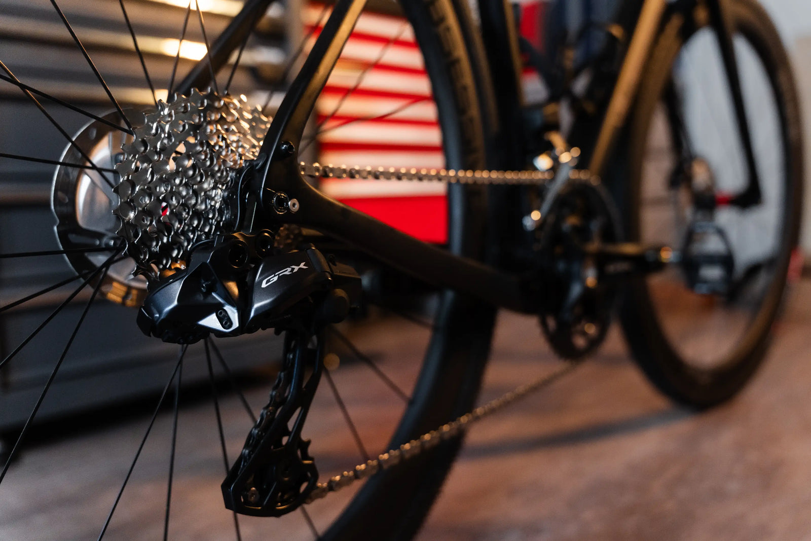 Close-up of Vélobsessive's Gravel Bike  rear derailleur and cassette, with the chainring and wheel partially visible in a workshop setting.