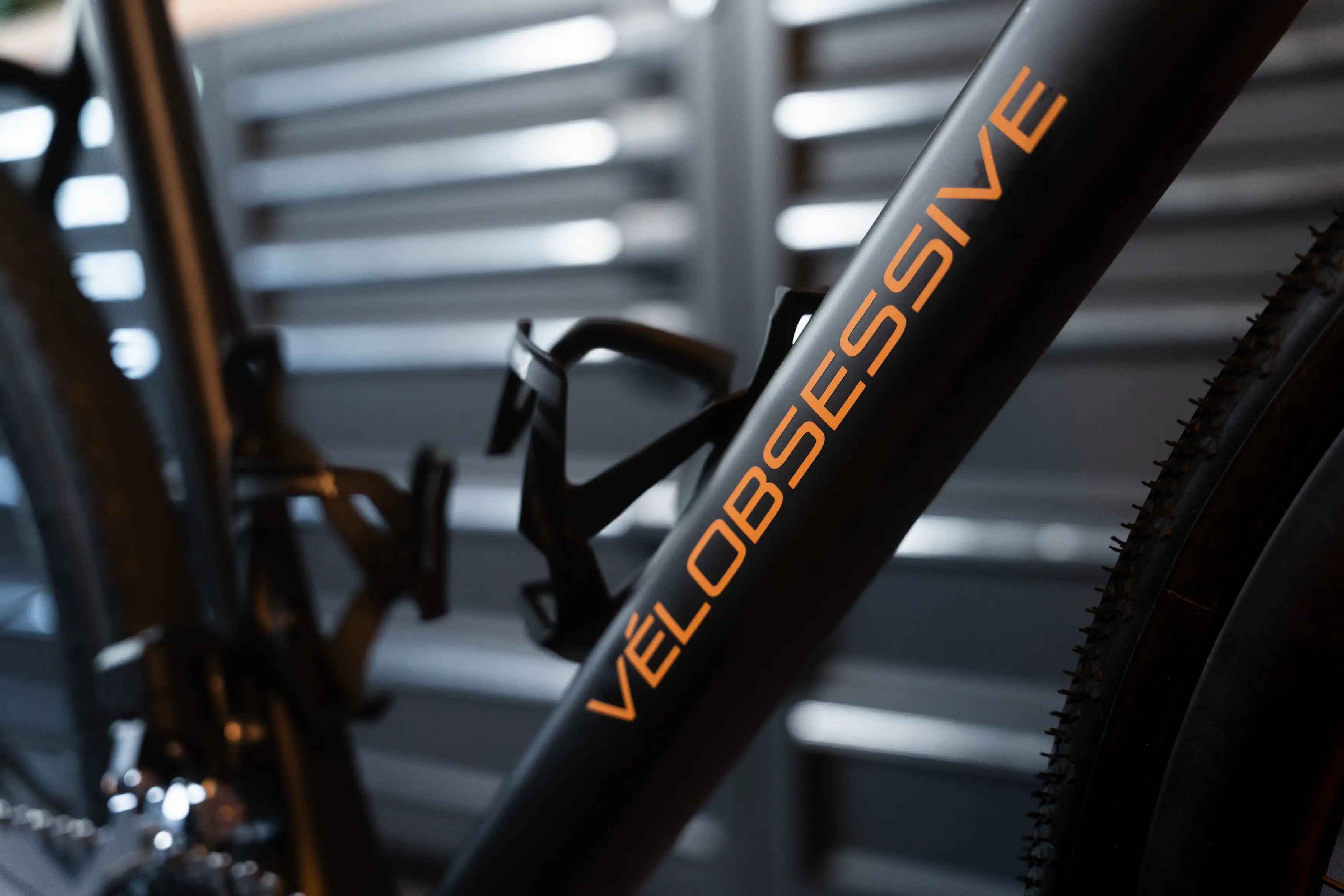Close-up of Vélobsessives Gravel BIKE Cobblestone frame with the word 'VELOOBSESIVE' printed in orange, with a black water bottle mounted on the frame.