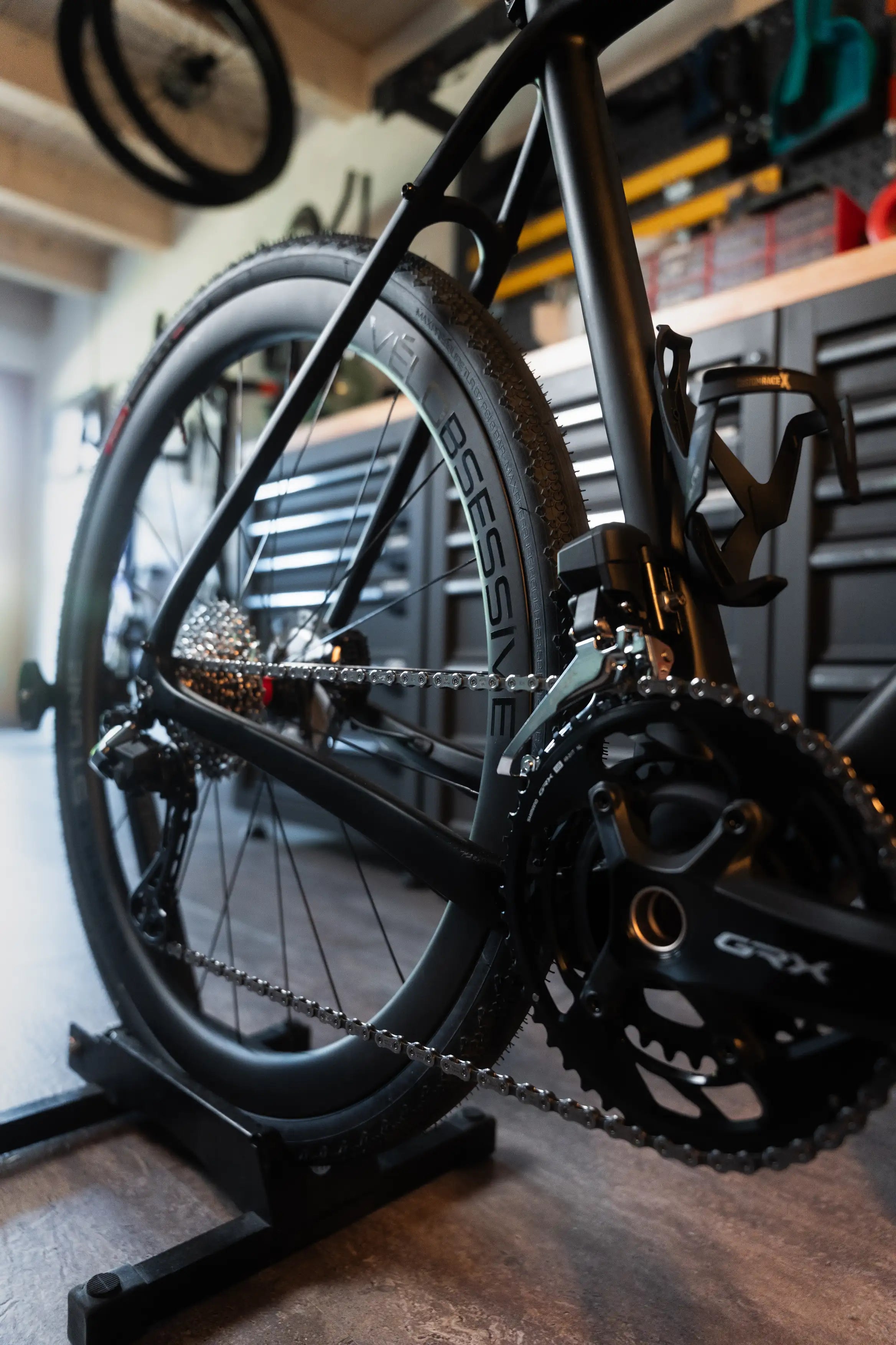 Close-up of Vélobsessive's Gravel Bike  rear wheel, chainring, and cassette mounted on a black stand in a workshop setting.